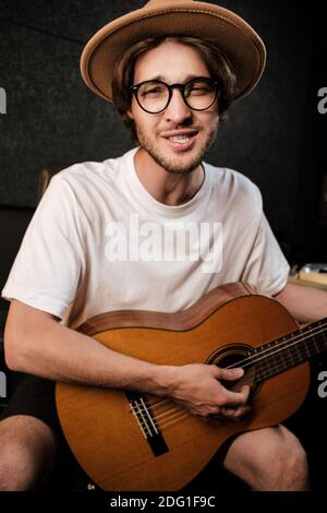 Portrait of attractive stylish man singing and playing on a guitar in recording studio Stock Photo