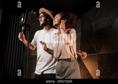 Young attractive man and woman joyfully singing together in sound recording studio. Two singers working in studio Stock Photo
