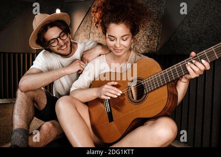 Young stylish musicians happily composing new song on guitar working together in sound recording studio Stock Photo