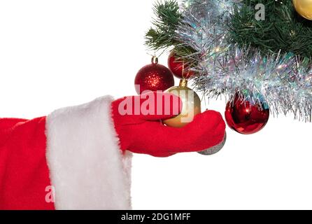 Santa Claus's hand holding a shiny golden ball hanging on decorated Christmas tree. Some other balls are out of focus. Winter holidays decoration conc Stock Photo