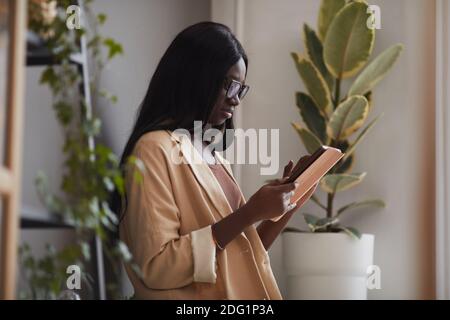 Side view portrait of successful African-American businesswoman using digital tablet while standing in eco friendly office, copy space Stock Photo