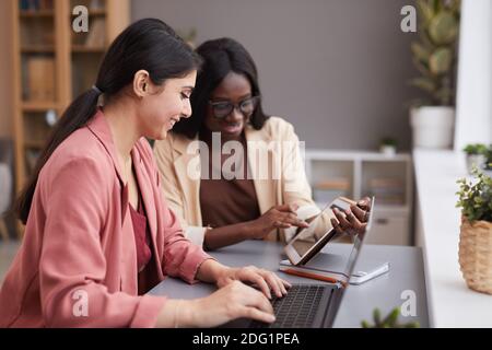 Side view portrait of two ethnic businesswomen using digital tablet during meeting while managing successful business together, copy space Stock Photo