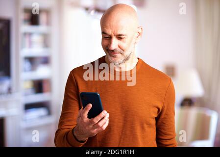 Shot of middle aged man using his mobile phone while standing in the living room at home. Stock Photo