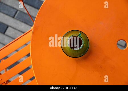morning coffee Alfresco in the park, green espresso coffee cup sitting on an orange cafe table Stock Photo