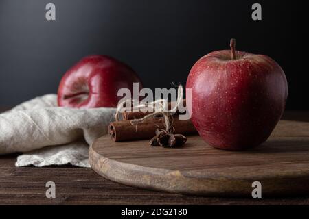 Red apples with cinnamon on cutting board on wooden table. Side view of fresh fruits. Stock Photo
