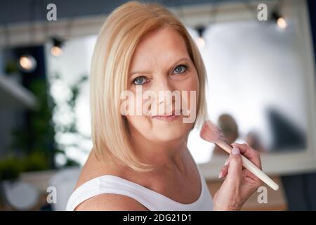 Senior woman applying makeup in the bathroom Stock Photo