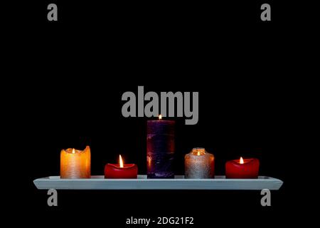 Colorful candles on a wooden shelf isolated on black background with copy space