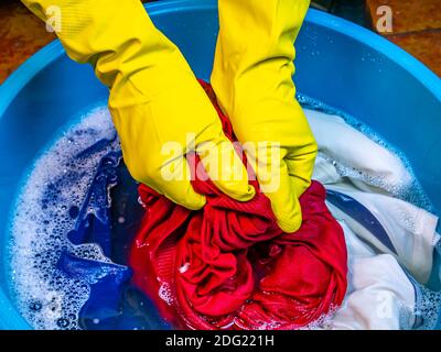 Hand wash clothes in a plastic bowl. Washing powder. Washer. Hand wash laundry in a plastic bowl. Household. Housekeeper. Female home drud. Handwork. Stock Photo