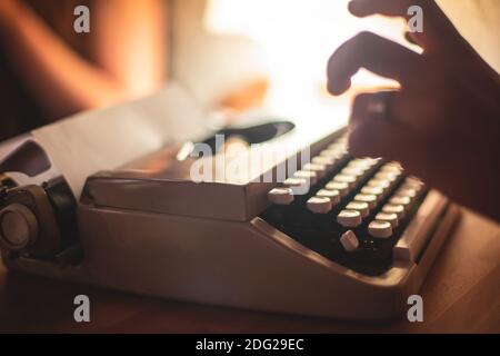 Process of writing a text letter on a white sheet of paper with old-fashioned typewriter, modern writer machine in warm room candle light, close up vi Stock Photo