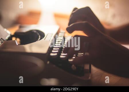Process of writing a text letter on a white sheet of paper with old-fashioned typewriter, modern writer machine in warm room candle light, close up vi Stock Photo
