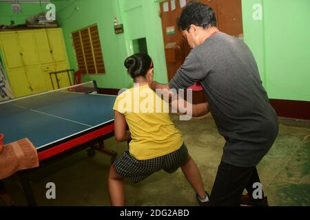 Kajol Dey, a 49 year old disabled table tennis player and coach is seen coaching a young girl at his coaching camp on International Day of Persons with Disabilities (IDPD). Agartala, Tripura, India. Stock Photo