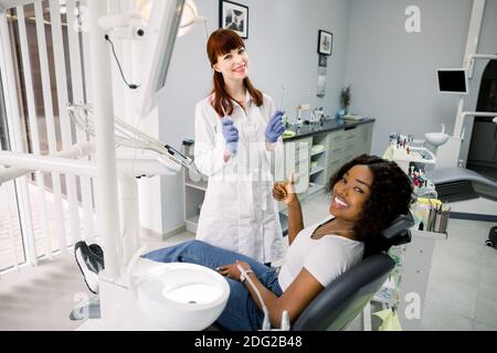 Healthy teeth and caries prevention concept. Young pretty African woman at the dentist's chair during a dental examination and treatment, showing Stock Photo