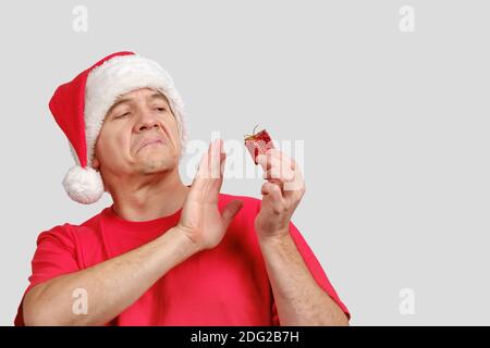 Disappointment middle-aged man in Santa hat holds bad small Christmas gift Stock Photo