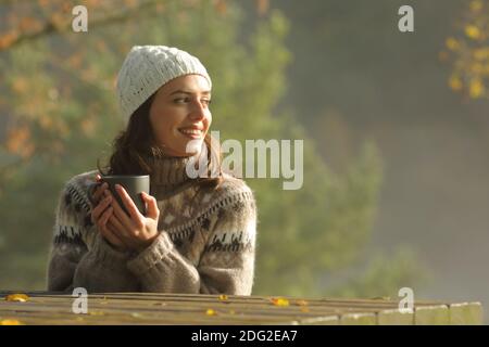 Happy woman drinking coffee looks at side sitting in a park in the morning Stock Photo