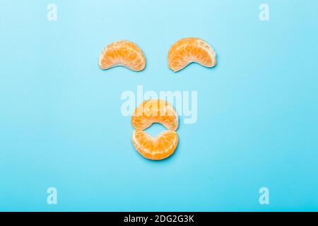 Tangerine slices on a blank colored minimal background. Funny face made of tangerine slices. Creativity and idea concept. Stock Photo