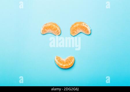 Tangerine slices on a blank colored minimal background. Funny face made of tangerine slices. Creativity and idea concept. Stock Photo