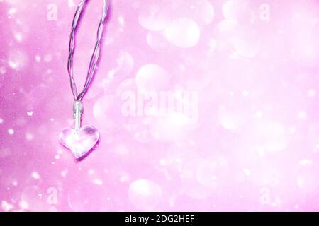 Small transparent glass heart on soft pink background with bokeh effect. Valentine's day symbol. Decorative element. Festive Valentine card. Stock Photo