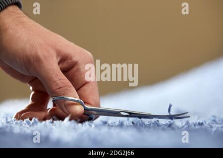 Closeup of hand cutting off string on a carpet with scissors. Carpet cleaning service Stock Photo