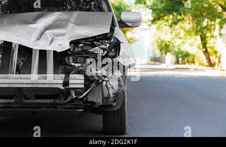 Destroyed car in car crash traffic accident on city road. Smashed broken auto headlight, dented hood without bumper in gray car accident with copy Stock Photo