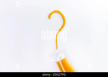 The bright yellow question mark is drawn with paint from the tube on a white background. Waiting for the announcement of the color of the year Stock Photo