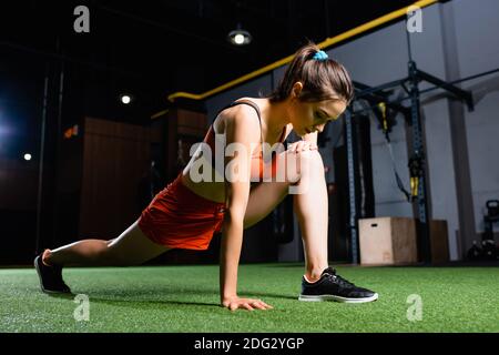 athletic sportswoman doing forward lunges exercise while warming up in gym Stock Photo