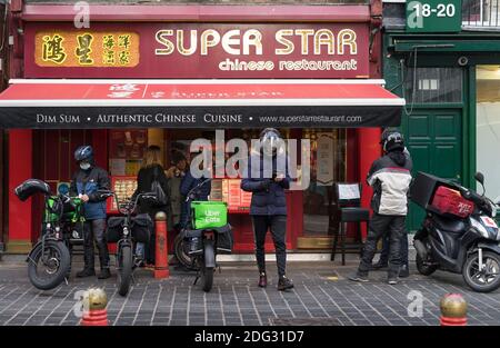 Uber Eats and Just Eat bike delivery riders wait outside a Chinese restaurant in Chinatown. London Stock Photo