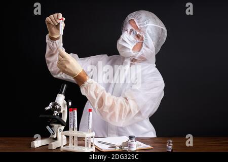 male scientist is testing a sample of biological tubes contaminated by Corona-virus Covid 19, using microscope Stock Photo