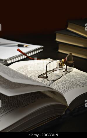 Open book and glasses located on a dark table and a dark background Stock Photo
