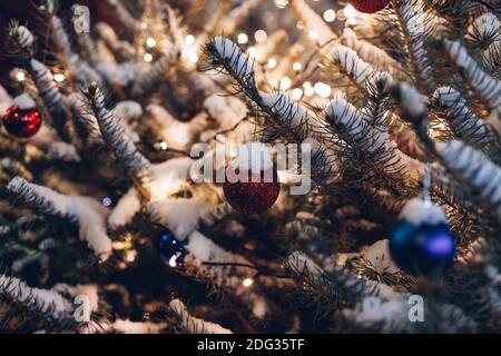 Outdoor Christmas tree decorated with ornaments and lights at night. Branches covered with snow. New year holiday celebration Stock Photo