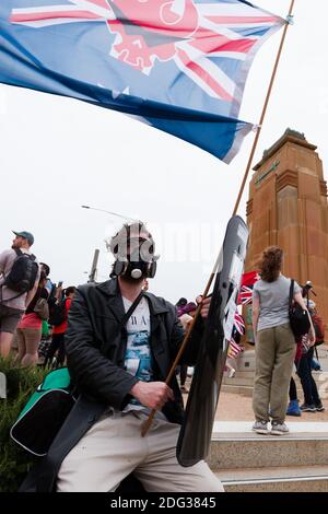 South Yarra, Australia, 5 December, 2020. A man in a gas mask holds up a mock flag during the Sack Daniel Andrews Protest in Fawkner Park. Parts of the community are looking to hold the Victorian Premier accountable for the failings of his government that led to more than 800 deaths during the Coronavirus crisis. Victoria has recorded 36 days Covid free as pressure mounts on the Premier Daniel Andrews to relax all remaining restrictions. Credit: Dave Hewison/Alamy Live News Stock Photo