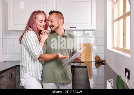 happy couple hold papers , checking utility bills or insurance. caucasian man and woman have talk, in the kitchen Stock Photo