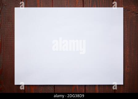 A sheet of white paper on a dark wooden background. Mockup for drawing. Copy Space for text. Stock Photo