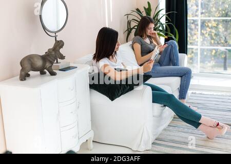 The girls are sitting on the couch looking at the phone and the book. Stock Photo