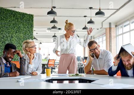 rude angry female boss executive is dissatisfied irritated by employees, scream at them, incompetent workers. in modern office Stock Photo