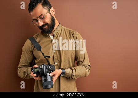 photographer with camera isolated on brown background, successful professional male looks at photos on screen of camera. photography concept Stock Photo