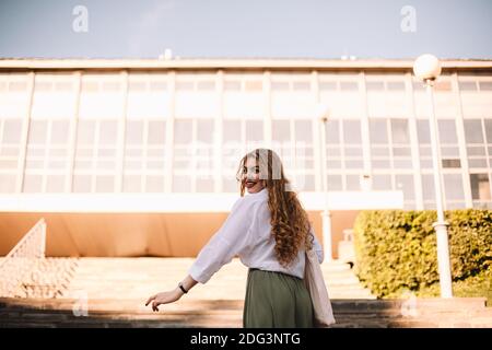 Happy young woman looking at camera while walking up stairs going to work Stock Photo