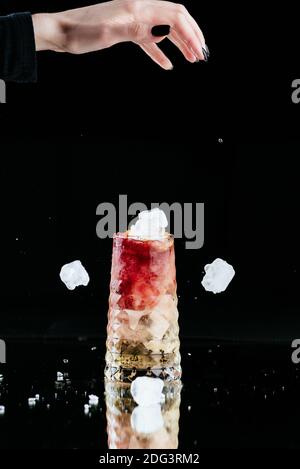 bright alcoholic cocktail on a black background and a woman's hand with falling ice Stock Photo