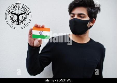 Indian man wear all black and face mask, hold India flag in hand isolated on white background with Uttar Pradesh state emblem . Coronavirus India stat Stock Photo