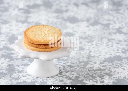 Fresh baked snowflake stamped sugar cookies on a white ceramic cake stand, and white and gray snowflake print tablecloth Stock Photo