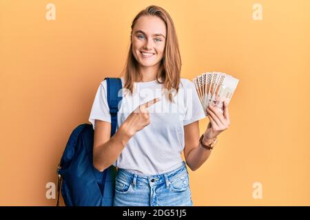 Beautiful blonde woman wearing student backpack and holding 5000 south korean won smiling happy pointing with hand and finger Stock Photo