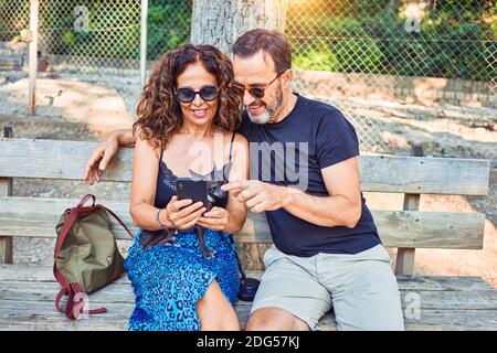 Middle age couple smiling happy using smartphone. Sitting on the bench with chihuahua dog at park Stock Photo