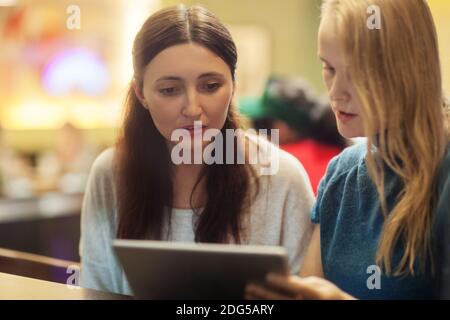 Two women have a discussion in the restaurant using electronic tablet Stock Photo