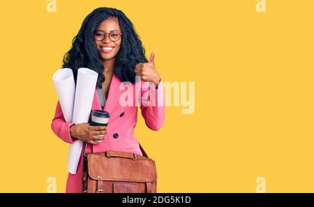 Beautiful african american woman holding paper blueprints and drinking coffee smiling happy and positive, thumb up doing excellent and approval sign Stock Photo