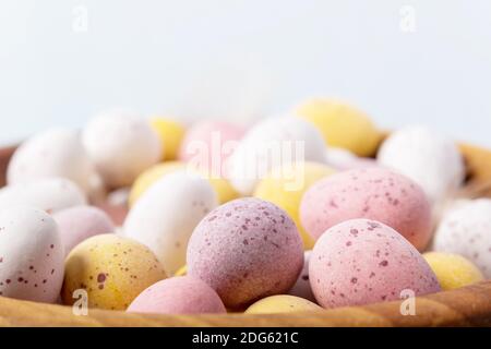 Close up Easter eggs in wooden bowl on blue background. Selective focus. Close-up. White yellow pink eggs for Easter treat. Stock Photo