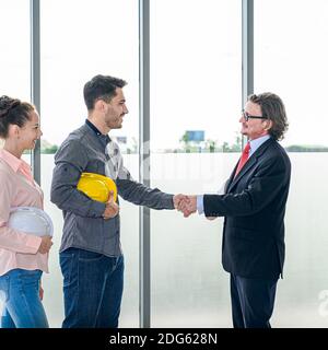 Two Caucasian architect or engineer holding helmet and smiling handshake for success project. Engineering business occupation. Stock Photo