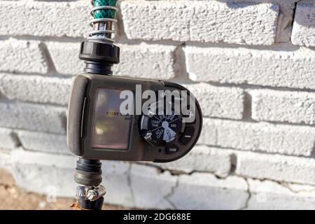 Alexandria, VA, USA 11-28-2020: Close up digital hose timer attached to garden hose coming out of a brick house. Inlet and outlet hoses are screwed in Stock Photo