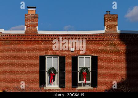 A vintage brick building with window decorations featuring pine Christmas wreaths with red ribbons.  The old house has two chimneys on top. Clear sky Stock Photo