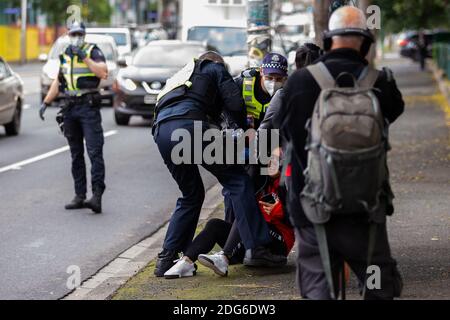 Melbourne, Australia, 7 July, 2020.  A woman standing on the street in support of the residents inside of 120 Racecourse road is violently slammed to the ground and arrested as police swarm on a small number of people amid the third full day of the total lockdown of 9 housing commission high rise towers in North Melbourne and Flemington during COVID 19 on 7 July, 2020 in Melbourne, Australia. After recording a horror 191 COVID-19 cases overnight forcing Premier Daniel Andrews to announce today that all of metropolitan Melbourne along with one regional centre, Mitchell Shire will once more go b Stock Photo