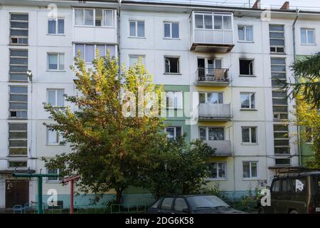 Fire in a residential, apartment building. Opened, broken windows of a burnt-out apartment, soot on the facade of the building. Stock Photo