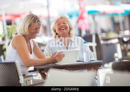 Senior women laughing while using tablet PC in cafe Stock Photo